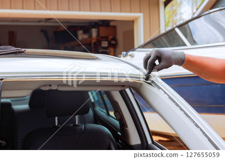 Worker works on sealing window trim of car in garage filled with car maintenance tools. 127655059
