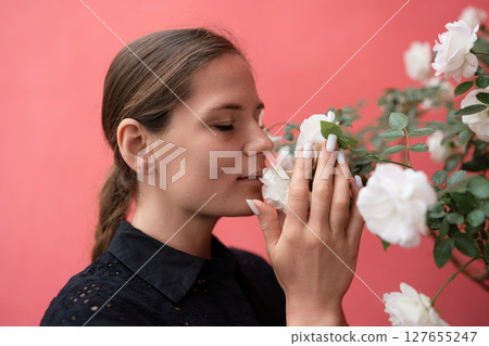Woman Roses Aroma: Young woman smelling white roses, with closed eyes, indoors, on coral background, for pleasure. 127655247