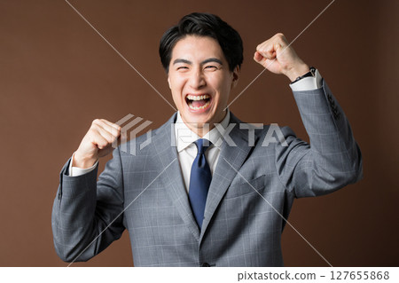 一位西裝革履的商人的上半身在棕色背景下揮舞著拳頭。專業人士或房地產主管的圖片 127655868