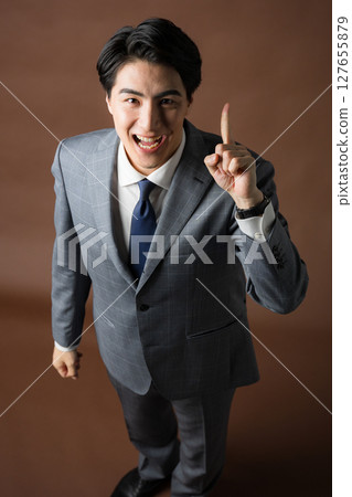 Businessman looking at camera and making pointing finger or no1 pose against brown background Businessman looking at camera and making pointing finger or no1 pose against brown background 127655879
