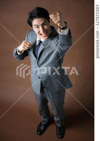 Full-body overhead view of a businessman in a suit pumping his fist against a brown background 127655883