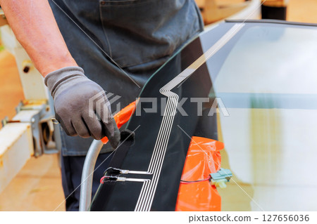 Technician carefully applies adhesive to edge of car windshield during installation windshield at workshop. Technician carefully applies adhesive to edge of car windshield during installation windshield at workshop. 127656036