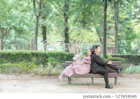 一對身穿粉紅色洋裝的夫妻坐在森林的長椅上拍婚紗照 127658040