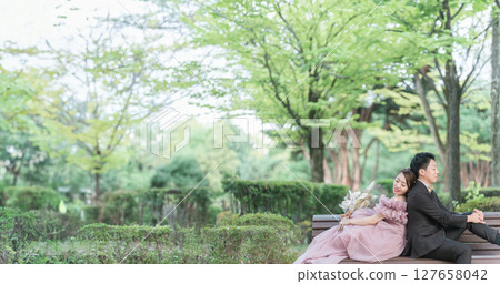 Couple in pink dresses taking wedding photos sitting on a bench in the forest 127658042