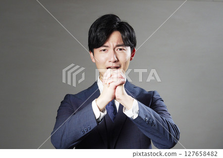 Businessman pleading, black background, looking at camera 127658482
