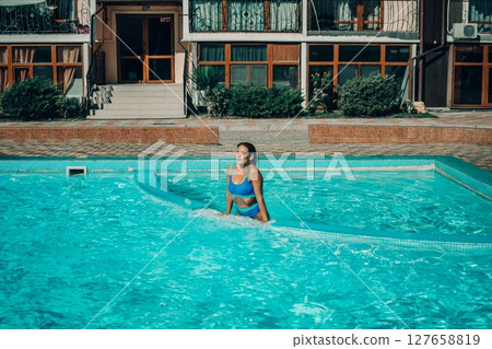 A woman is in the water, smiling and enjoying herself. The water is blue and the pool is surrounded by a white ledge. 127658819