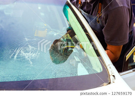Technician works on fixing scratched windshield with specialized tools, replace windshield precision in garage. Technician works on fixing scratched windshield with specialized tools, replace windshield precision in garage. 127659170
