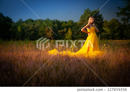 A Beautiful and Elegant Woman Dressed in a Lovely Yellow Dress in a Serene Green Field 127659356