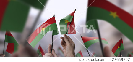 Burkina Faso flags in their hands on a blurred urban background 127659707