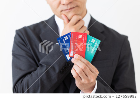 A businessman in a suit holding a credit card and worrying A businessman in a suit holding a credit card and worrying 127659982