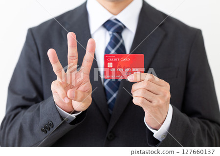 一位西裝革履的商人，手裡拿著信用卡，伸出三根手指 127660137