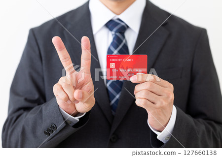 A businessman in a suit making a peace sign while holding a credit card 127660138