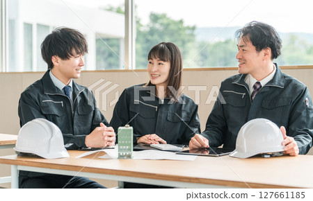 Male and female businessmen in work clothes having a meeting while looking at a model of a building 127661185