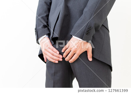 A middle-aged male businessman in a suit suffering while holding his buttocks 127661399