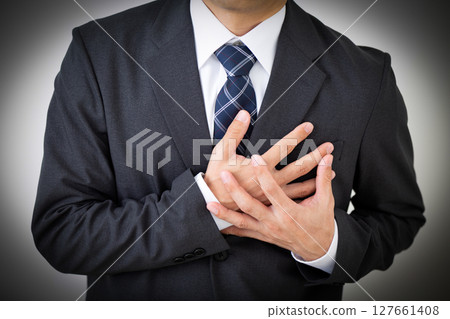 A middle-aged male businessman in a suit suffering while holding his chest 127661408