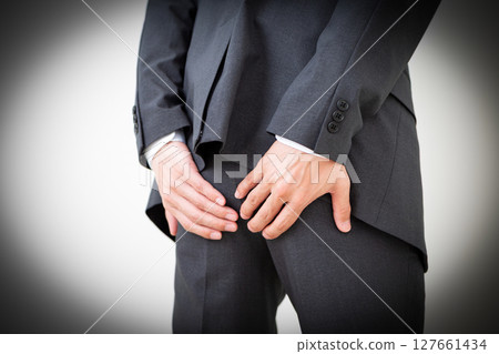 A middle-aged male businessman in a suit suffering while holding his buttocks 127661434