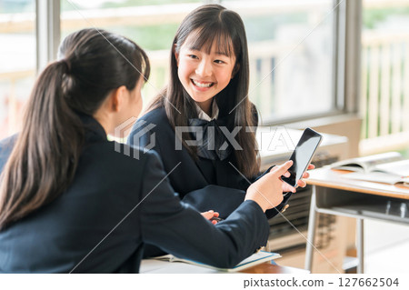 A female junior high school student talking while looking at her smartphone in a school classroom 127662504