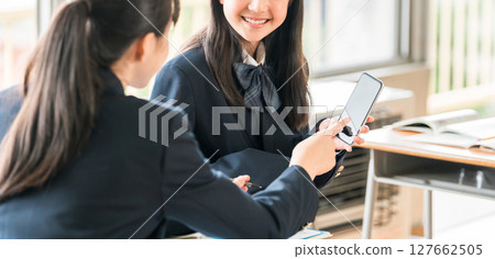 A female junior high school student talking while looking at her smartphone in a school classroom 127662505
