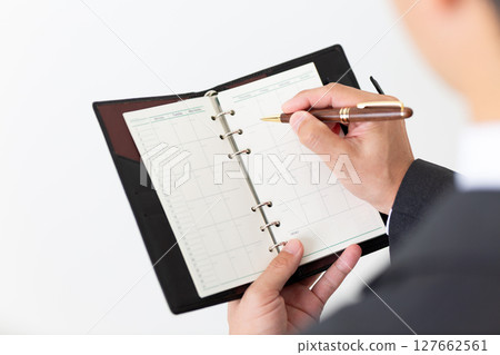 A middle-aged male businessman in a suit holding a black notebook A middle-aged male businessman in a suit holding a black notebook 127662561