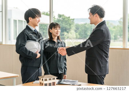 A young Asian man in work clothes and a businessman in a suit shaking hands in a conference room A young Asian man in work clothes and a businessman in a suit shaking hands in a conference room 127663217