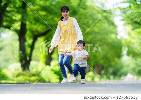 A female nursery teacher and a one-year-old boy playing in a park with fresh greenery A female nursery teacher and a one-year-old boy playing in a park with fresh greenery 127663618