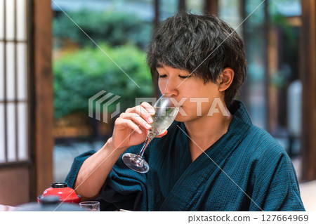 Asian man in yukata drinking aperitif, champagne, sparkling wine at meal in ryokan, hot spring inn 127664969
