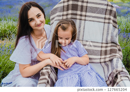 A rocking chair with a checkered blanket stands among purple flowers 127665204
