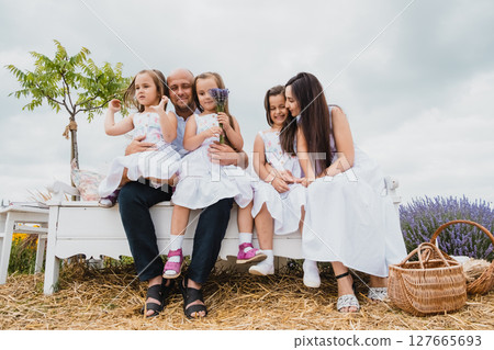 A close-knit family sits on an old-fashioned bench in a picturesque field A close-knit family sits on an old-fashioned bench in a picturesque field 127665693