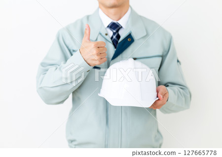 A middle-aged male businessman wearing green work clothes, holding a helmet and giving a thumbs up 127665778