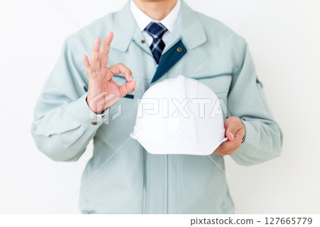 A middle-aged male businessman wearing green work clothes, holding a helmet and making a circle sign A middle-aged male businessman wearing green work clothes, holding a helmet and making a circle sign 127665779