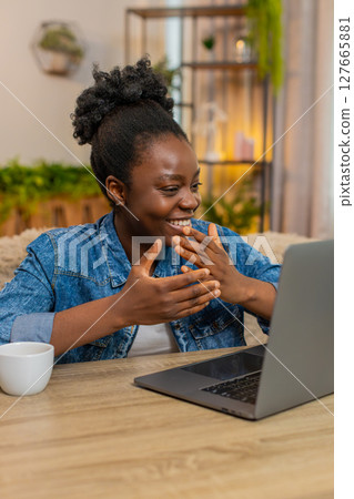 African American woman waving hand while chatting with friends conversation online on laptop at home 127665881