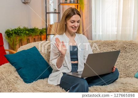 Adult woman waving during video call on laptop at home, recording vlog or teaching online class 127665898