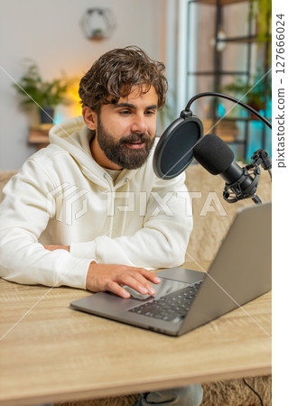 Happy Indian blogger man recording podcast on sofa, giving workshop, webinar sitting on sofa at home Happy Indian blogger man recording podcast on sofa, giving workshop, webinar sitting on sofa at home 127666024