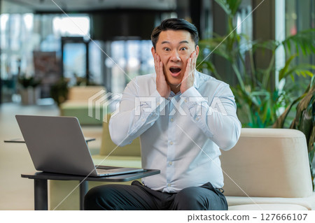 Chinese young businessman in shirt looking at camera shocked by sudden victory in office lobby Chinese young businessman in shirt looking at camera shocked by sudden victory in office lobby 127666107