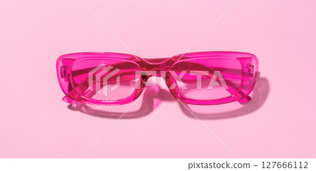 Stylish pink plastic sunglasses with transparent glass on a pink background 127666112