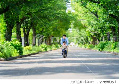 A 5-year-old boy practices riding a bicycle with his father following him 127666391