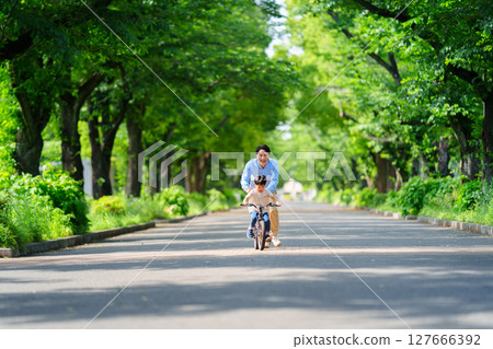 A 5-year-old boy practices riding a bicycle with his father following him A 5-year-old boy practices riding a bicycle with his father following him 127666392