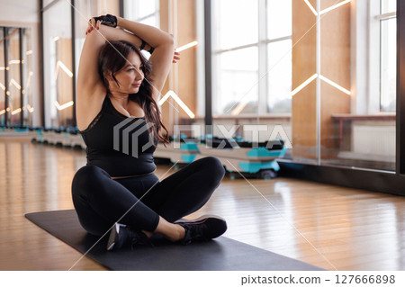 Plus-size woman stretching on yoga mat in gym, embracing self-care and body positivity.. Plus-size woman stretching on yoga mat in gym, embracing self-care and body positivity.. 127666898