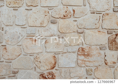 Background image of a decorative stone wall made of roughly processed limestone blocks of different shapes and sizes. Stones of light beige and cream shades. Texture of stone wall 127666967