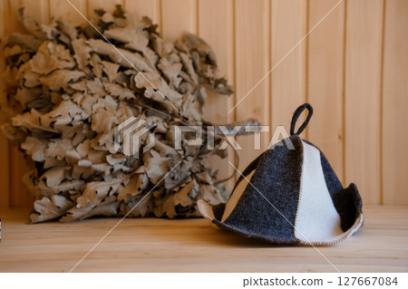 Traditional Finnish Sauna Scene with Birch Branches and Ushanka Hat on Wooden Surface, Rustic Texture, Dark and Light Gray Tones Traditional Finnish Sauna Scene with Birch Branches and Ushanka Hat on Wooden Surface, Rustic Texture, Dark and Light Gray Tones 127667084