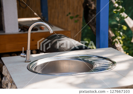Outdoor Kitchen Sink with Modern Faucet, Rustic Counter, Wood Cabinet and Blue Accents: Bright Summertime Scene Outdoor Kitchen Sink with Modern Faucet, Rustic Counter, Wood Cabinet and Blue Accents: Bright Summertime Scene 127667103