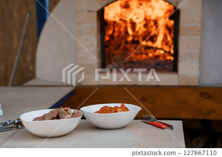 Rustic Wood-Fired Oven Cooking: Two Bowls of Stew and Burning Flames Inside Brick Kitchen Hearth, Warm Orange Tones and Cozy Style Rustic Wood-Fired Oven Cooking: Two Bowls of Stew and Burning Flames Inside Brick Kitchen Hearth, Warm Orange Tones and Cozy Style 127667110