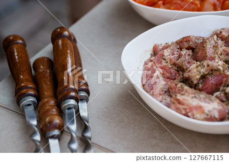 Raw Lamb Meat Preparation with Carving Knives. Close-up Culinary Scene Featuring Seasoned Meat in White Bowls, Rustic Wood and Metal Tools. 127667115