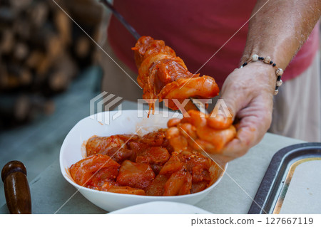 Spicy Adana Kebab Preparation: Hands Skewering Marinated Meat with Red Pepper Paste, Outdoor Grill Scene Spicy Adana Kebab Preparation: Hands Skewering Marinated Meat with Red Pepper Paste, Outdoor Grill Scene 127667119