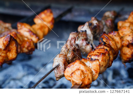 Sizzling Kebabs on Charcoal Grill: Close-Up View of Marinated Meat Skewers, Rustic Food Photography, Brown and Orange Tones, Dark Background 127667141