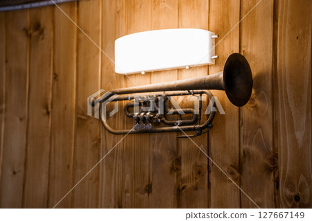 Unique Wall Sconce Crafted from Antique Brass Trumpet with Warm Lighting, Wooden Panel Background, Rustic Home Decor, Vintage Musical Instrument Design. 127667149
