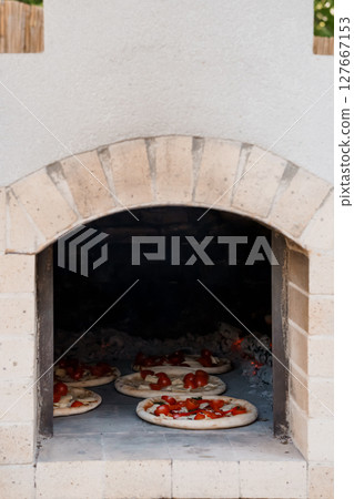 Rustic Stone Wood-Fired Pizza Oven with Margheritas Cooking Inside, Outdoor Kitchen, Warm Lighting, Traditional Italian Cuisine, Textured Stone Rustic Stone Wood-Fired Pizza Oven with Margheritas Cooking Inside, Outdoor Kitchen, Warm Lighting, Traditional Italian Cuisine, Textured Stone 127667153