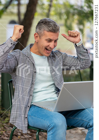 Happy man freelancer working on laptop screams in triumph win celebrating success sitting on chair Happy man freelancer working on laptop screams in triumph win celebrating success sitting on chair 127667231