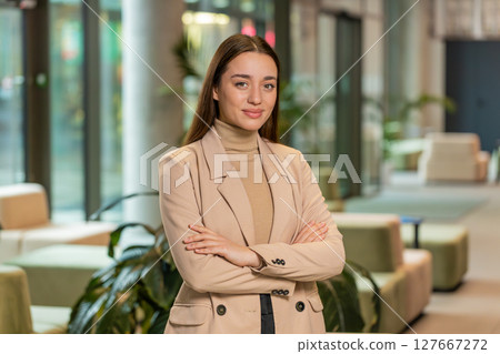 Portrait of happy young businesswoman with arms crossed looking at camera in office hotel lobby Portrait of happy young businesswoman with arms crossed looking at camera in office hotel lobby 127667272