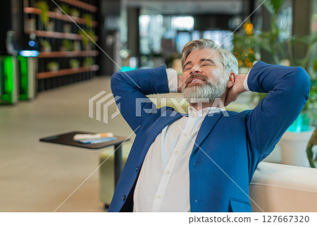 Caucasian businessman taking break leaning on couch after working celebrating success at hotel lobby Caucasian businessman taking break leaning on couch after working celebrating success at hotel lobby 127667320